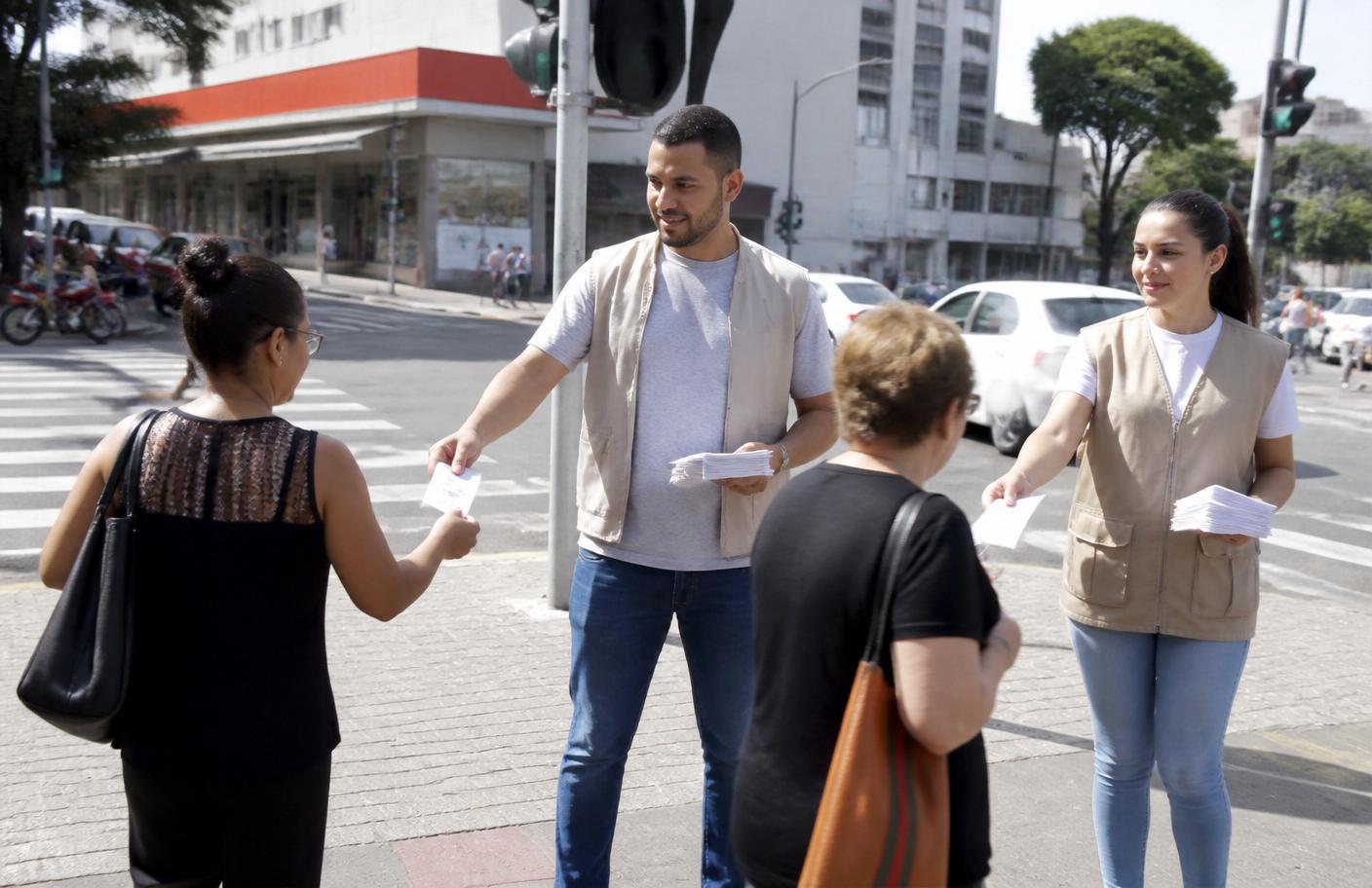 Equipe entregando material impresso genérico para pedestres em cruzamento urbano